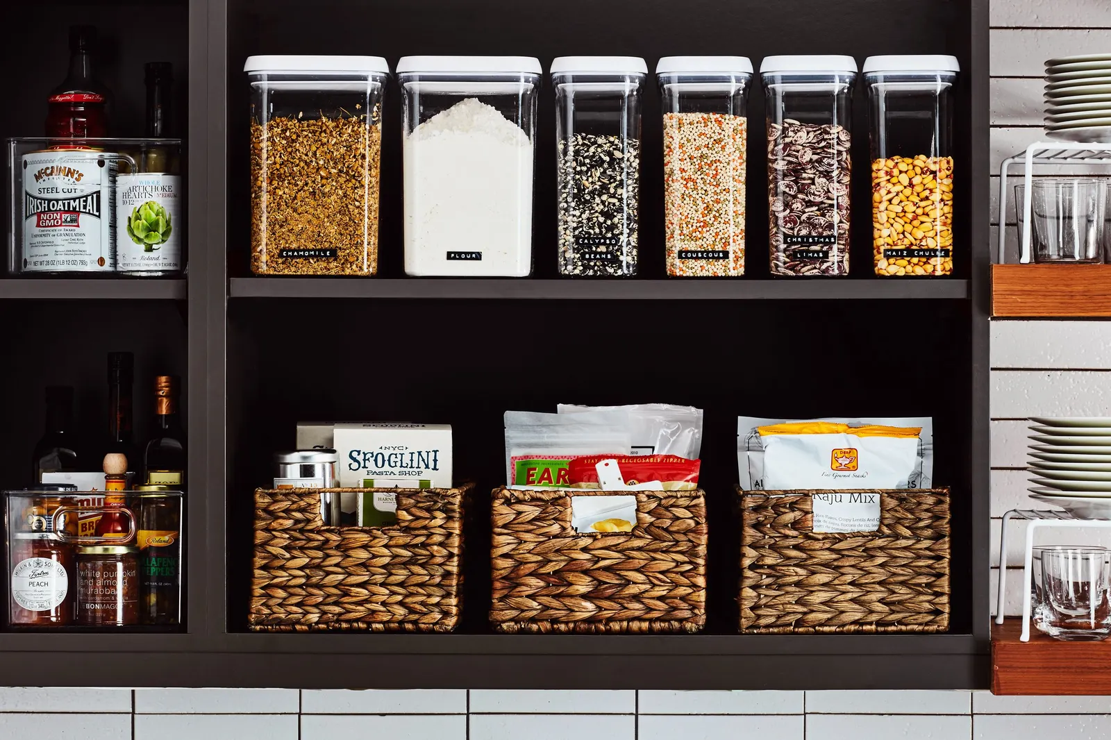 Organized pantry shelves with labeled canisters, woven baskets and glass jars