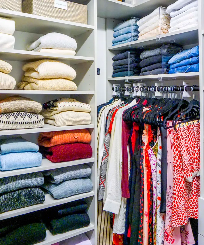 Neatly organized closet with folded sweaters on shelves and hung clothes behind dividers