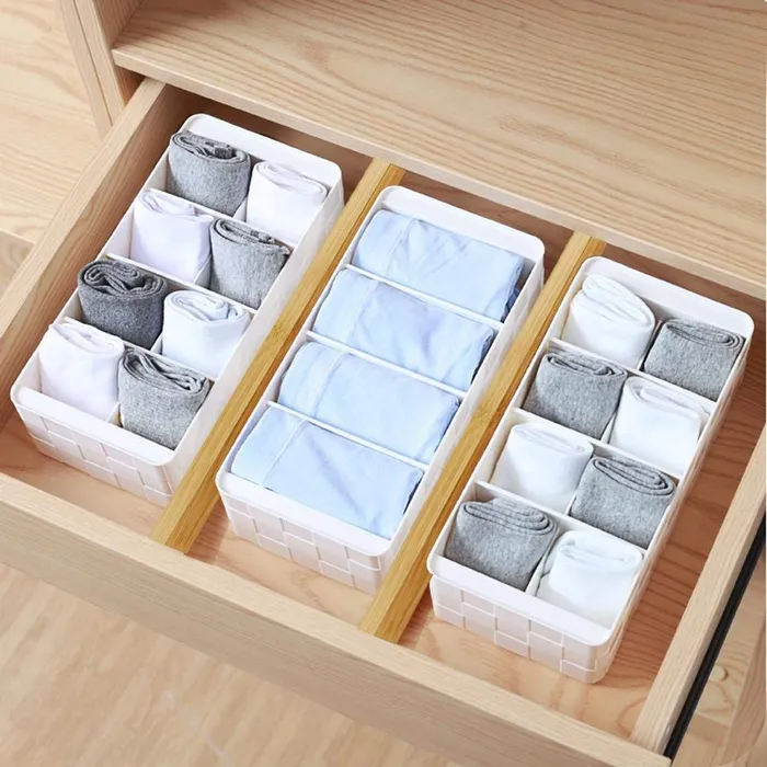 Wooden drawer fitted with white compartment organizer boxes and folded clothes