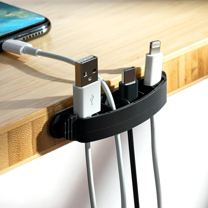 Bamboo cable organizer clipped to a desk edge holding charging cables beside a phone